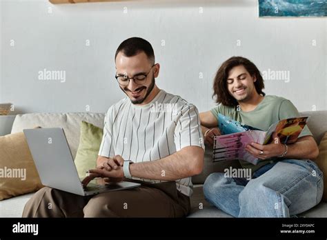 A Gay Couple Relaxes At Home One Working On A Laptop The Other Reading A Magazine Stock Photo