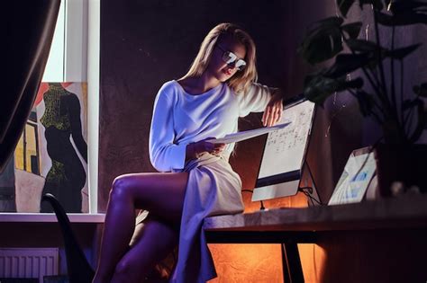 Sexy Blonde Frau Sitzt Auf Dem Tisch Und Liest Wichtige Dokumente Kostenlose Foto