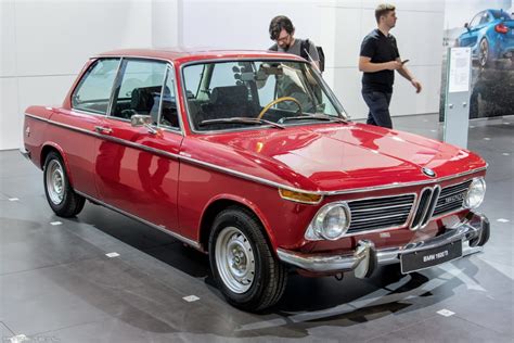 two men standing next to an old red car on display at a museum or showroom