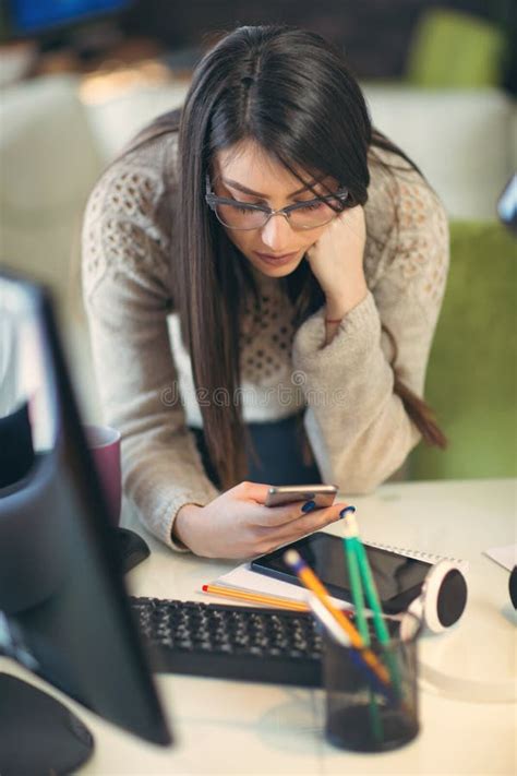 Woman Leaning Over The Desk In Home Office Using Smart Phone Stock