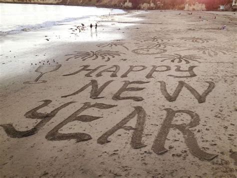 happy new year written in sand on the beach with people walking around ...