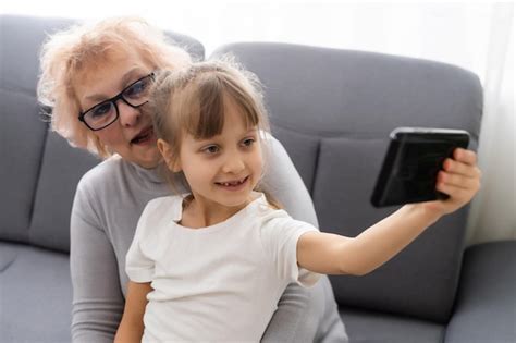 Abuela feliz y nieta usando el teléfono juntas sentadas en un cómodo