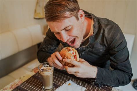 Happy Man Is Eating Fast Food Hamburger A Man Is Sitting At The Table