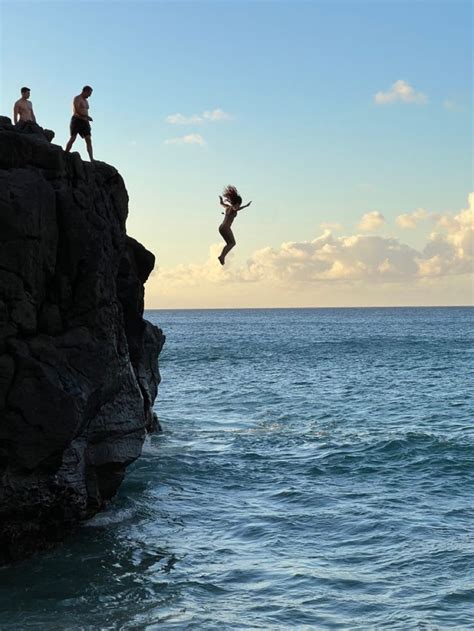 Two People Jumping Off Rocks Into The Ocean From A Cliff In The Middle