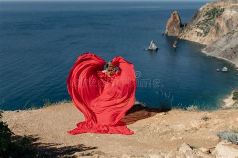 A Woman In A Red Dress Is Standing On A Rocky Beach With The Ocean In The Background The Woman