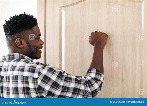 Side View Of African Guy Knocking Standing Near Closed Door Stock Photo