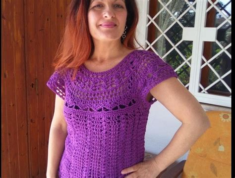 A Woman Wearing A Purple Crochet Top Standing In Front Of A Window