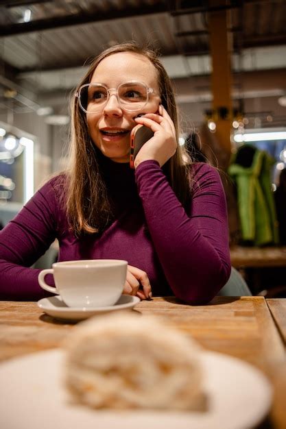 Una mujer está sentada en una mesa conversando en su teléfono celular