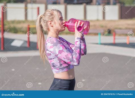 Beautiful And Athletic Blonde Girl Drinks Water After Jogging Stock