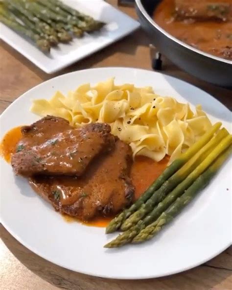 A White Plate Topped With Meat Pasta And Asparagus Next To Other Food