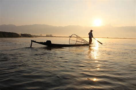 Silhouette Of A Fisherman On Boat Holding Paddle In Body Of Water