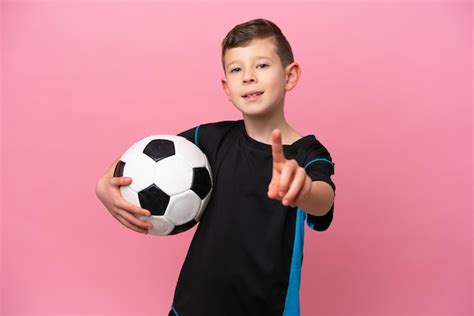 Pequeño jugador de fútbol caucásico aislado de fondo rosa mostrando y