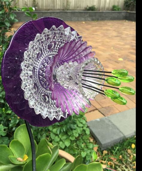 A Purple Flower Sitting On Top Of A Lush Green Plant Next To A Brick