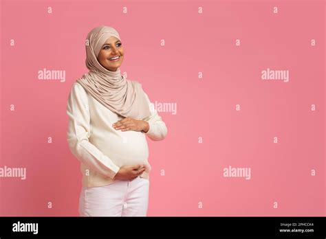 Pregnant Muslim Woman In Hijab Embracing Her Belly And Looking Away