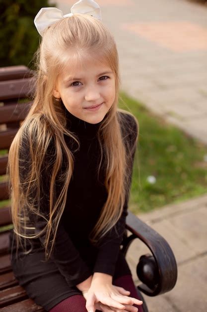 Premium Photo A Beautiful Blonde Girl With Long Hair In A Black Dress Is Sitting On A Park Bench