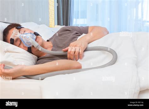 Asian Man Wearing Cpap Mask Connecting To Air Hose Sleeping On His Bed In His Bedroom With