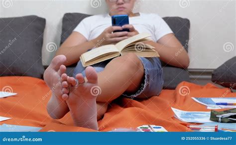 Teen In Glasses With A Smartphone In Hands And Open Book Studying