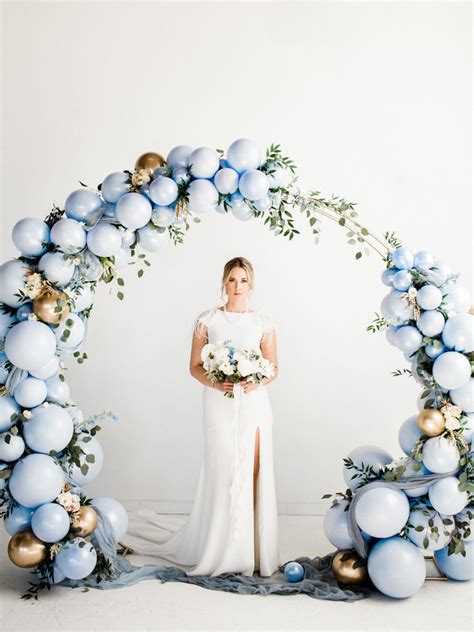 A Woman Standing In Front Of A White Backdrop With Blue And Gold Balloons