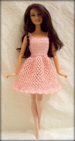 A Doll Wearing A Pink Crocheted Dress And Tights Is Posed On A White