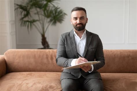 Portrait Of Confident Male Therapist In Suit Sitting On Couch Stock