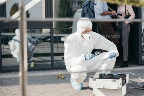 Male Criminologist In Protective Suit And Latex Gloves Looking Through