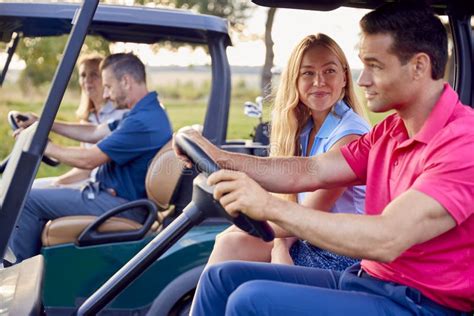 Mature And Mid Adult Couples Driving Buggies Playing Round On Golf