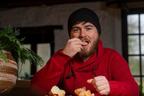 Premium Photo A Man In A Hat And Sweater Eats A Tangerine