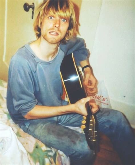 A Man Sitting On Top Of A Bed With A Guitar In His Hand And Looking At