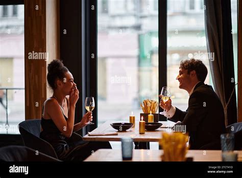 Happy Interracial Couple In Elegant Attire Holding Glasses Of Wine