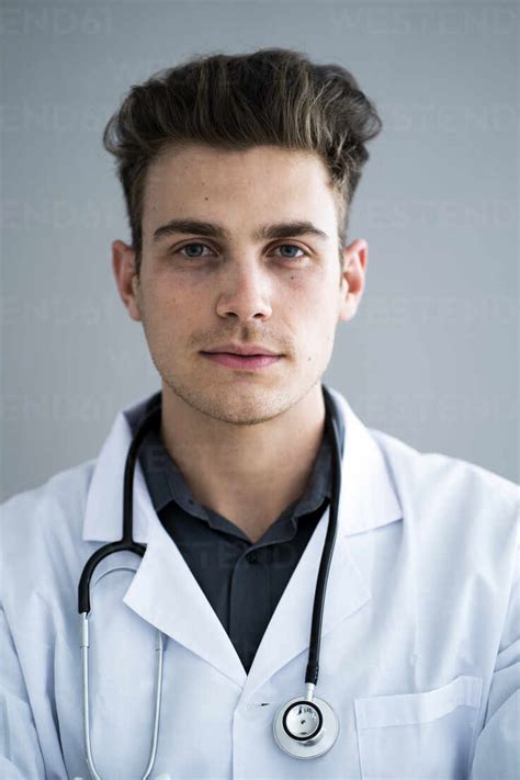 Handsome Male Doctor Against Gray Wall In Hospital Stock Photo