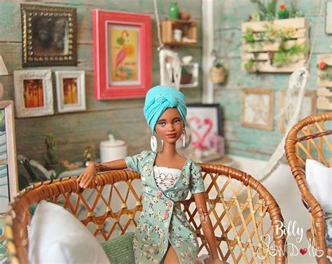 A Doll Is Sitting On A Wicker Chair In Front Of A Wall With Pictures