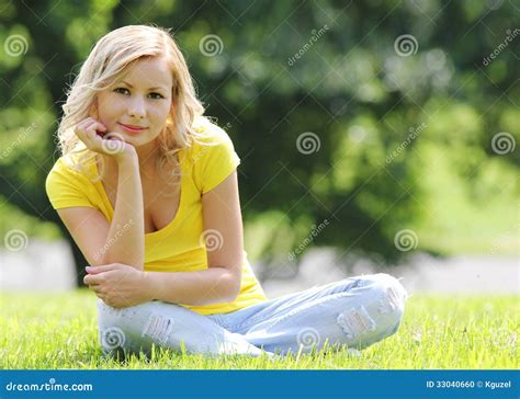 Blonde Girl Sitting On The Grass And Smiling Looking At The Camera