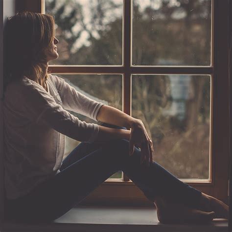 Young Attractive Woman Sitting On A Window Looking Outside Lonely