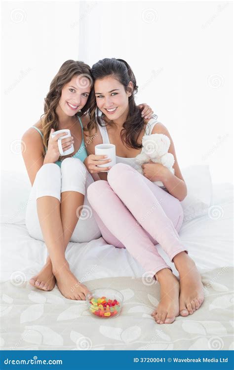 Cheerful Young Female Friends With Coffee Cups In Bed Stock Image