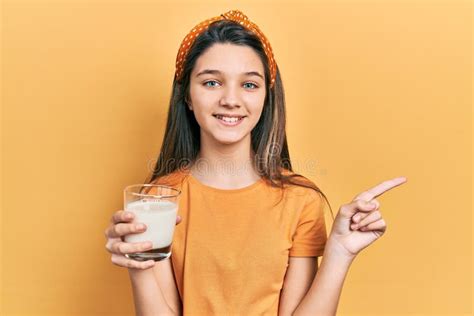 Young Brunette Girl Drinking A Glass Of Milk Smiling Happy Pointing