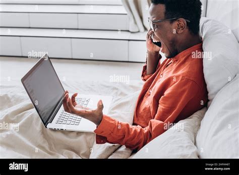 Excited African American Man In Orange Shirt And Glasses Talks On