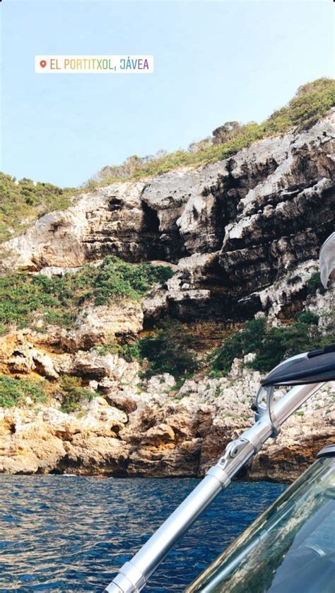 A Man Sitting On Top Of A Boat In The Ocean Next To A Rocky Cliff