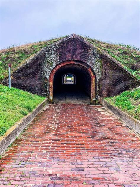 an old brick tunnel with grass growing on the roof and walkway leading up to it