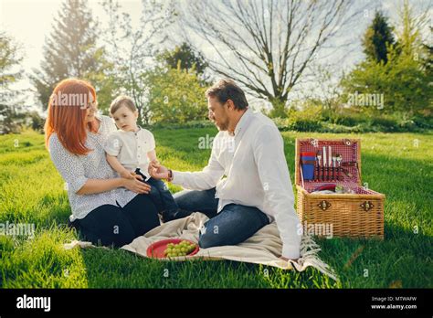 Beautiful And Stylish Redhead Mom In A White Blouse Sits On The Grass