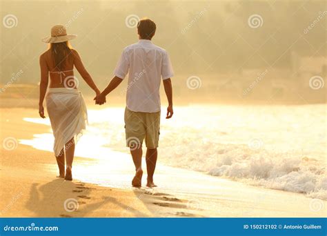 Back View Of A Couple Walking On The Beach At Sunrise Stock Photo