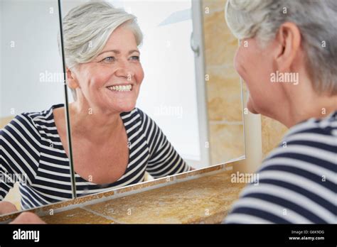 Portrait Of Smiling Woman Watching Herself In Bathroom Mirror Stock