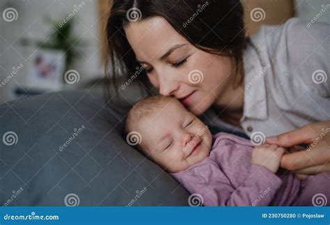 Happy Young Mother Kissing Her Newborn Baby Girl Lying On Sofa Indoors