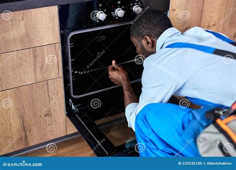 Young African Handyman Examining Electric Oven In Kitchen At Home