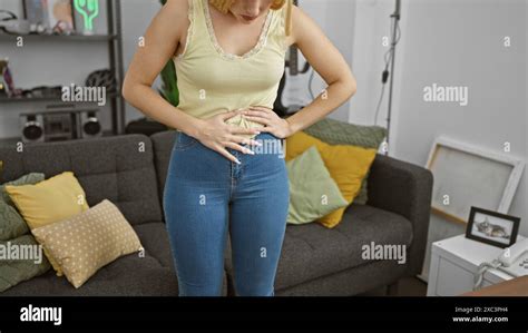 Blonde Woman In Casual Attire Standing Indoors Experiencing Stomach