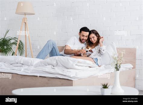 Smiling Interracial Couple Cuddling Jack Russell Terrier In Bed Stock