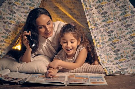 Mãe e filha estão sentadas em uma tenda lendo histórias a lanterna