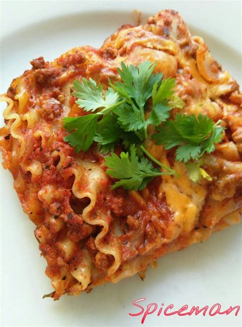 A White Plate Topped With Lasagna Covered In Sauce And Cheese Garnished With Cilantro