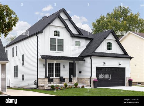 A traditional modern farmhouse with white siding, black roof and garage ...