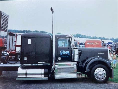 A Black Semi Truck Parked On Top Of A Grass Covered Field Next To Other