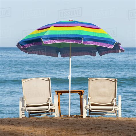 A Rainbow Beach Umbrella Over Two Lounge Chairs On The Beach At The